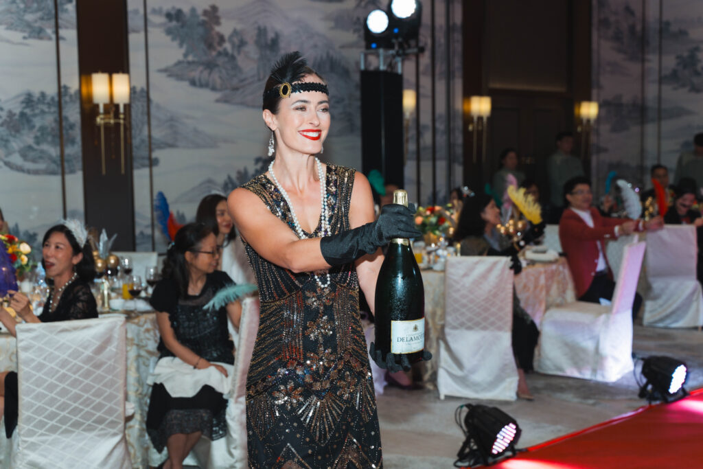 Bailarines Gatsby de CHRIO Entertainment sorprendiendo a un ganador con una botella Magnum de champán en el escenario de un evento corporativo en Hong Kong.